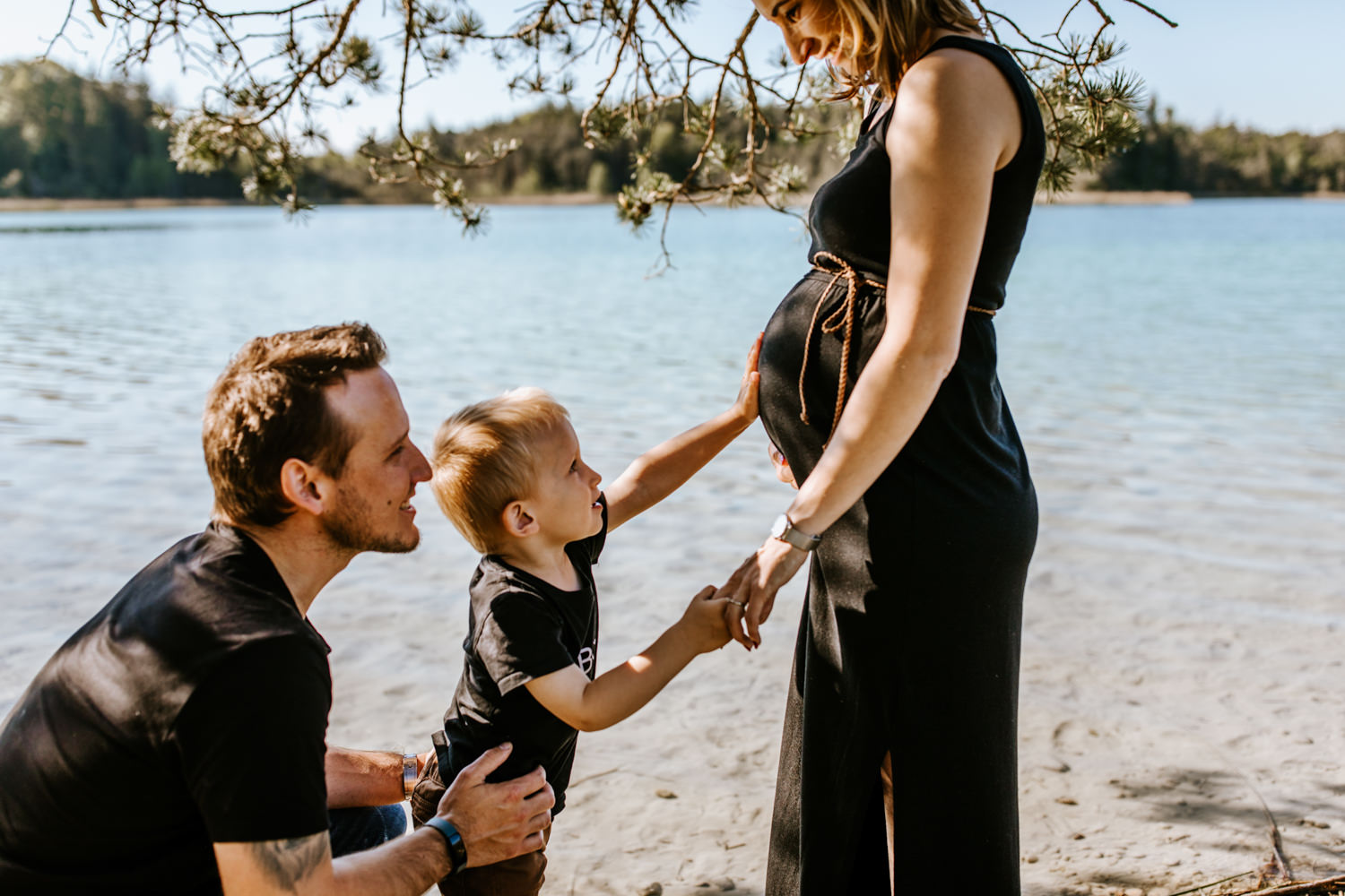 Sohn fasst Babybauch von Mama an am See Fotograf