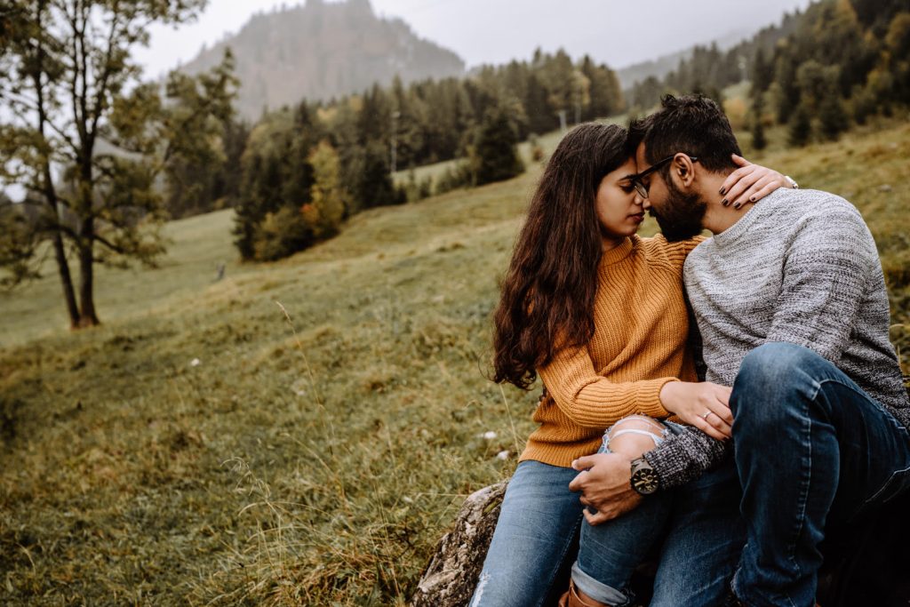 Verliebtes Paar schaut sich innig an - Couple sitzt auf Baumstumpf am Fuße eines Berges im Allgäu