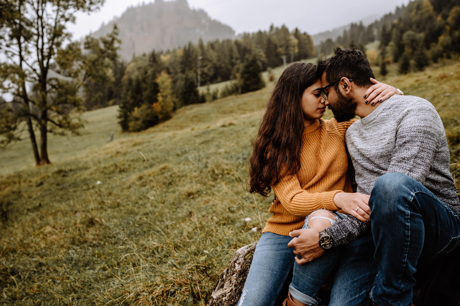 Verliebtes Paar schaut sich innig an - Couple sitzt auf Baumstumpf am Fuße eines Berges im Allgäu