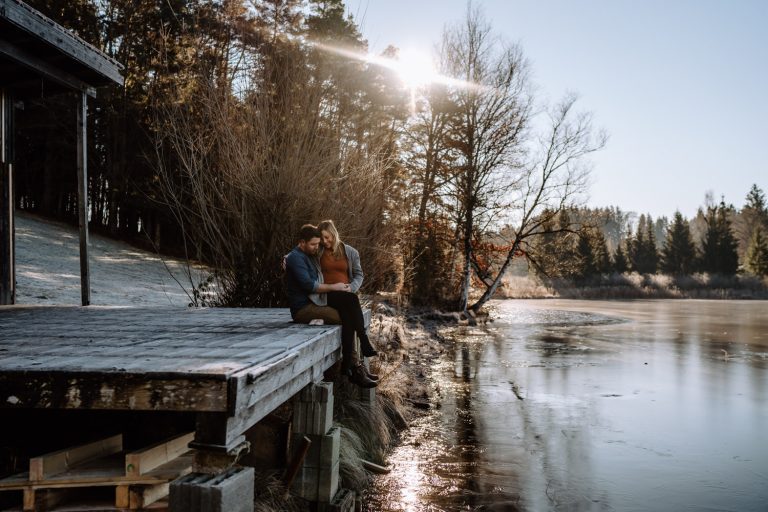 Babybauchfotos auf einem Steg mit Stadl am zugefrorenen See mit wunderschöner Sonne - Fotograf Weilheim