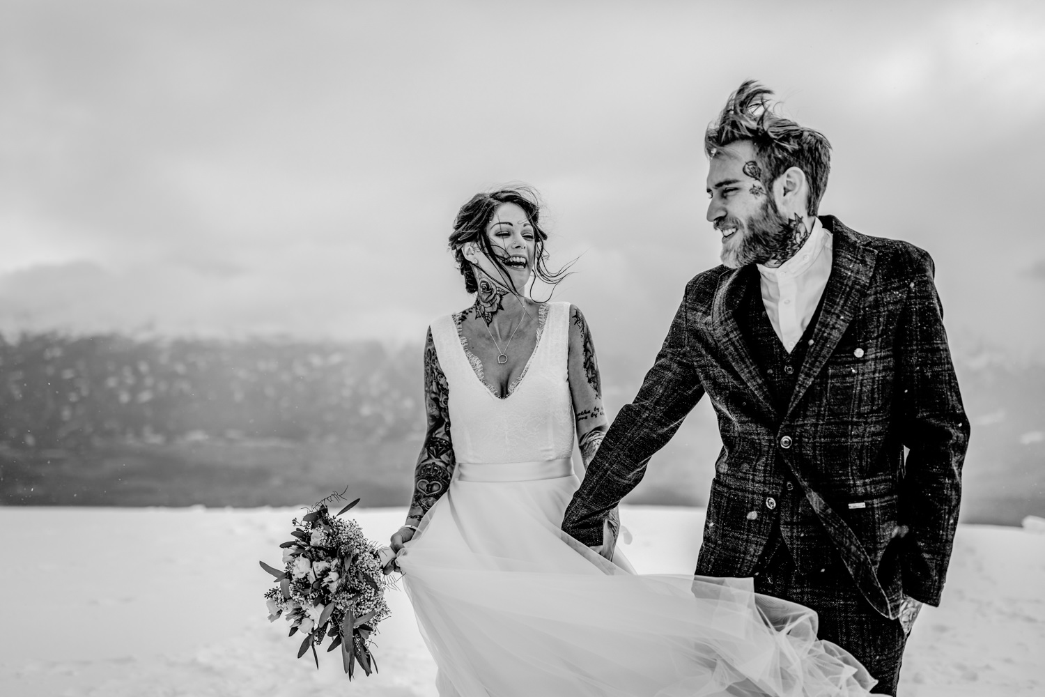 Braut und Bräutigam laufen Hand und Hand auf dem Gipfel im Schnee in schwarz weiß