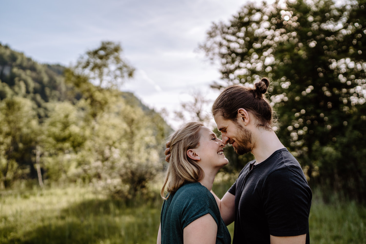 Couple sieht sich verliebt in die Augen auf einer Wiese mit Bergpanorama am Schwansee