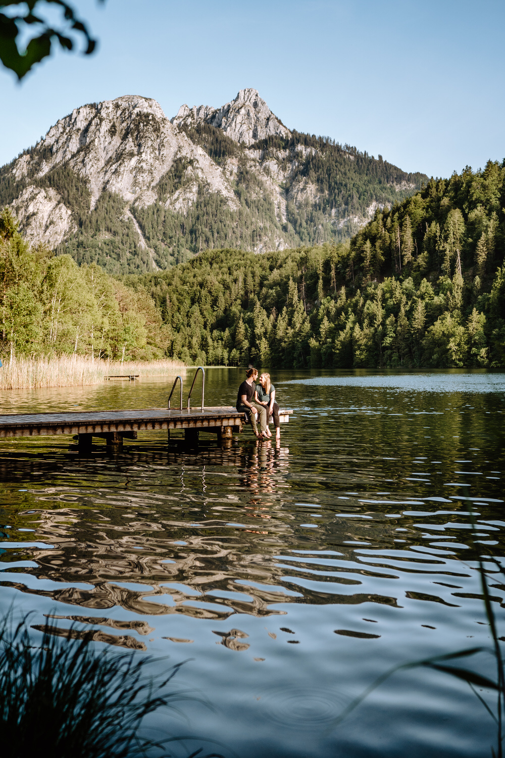 Babybauchfotos am Schwansee - Pärchen sitzt auf einem Steg und lässt die Füße ins Wasser baumeln