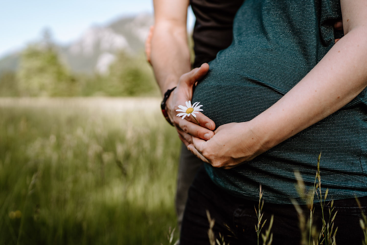 Babybauchfotos mit Blume vor dem Bauch auf einem Feld am Schwansee