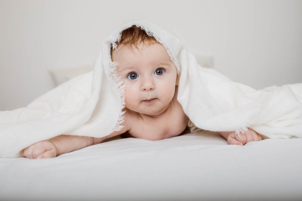 Baby schaut unter der Decke beim Babyshooting hervor