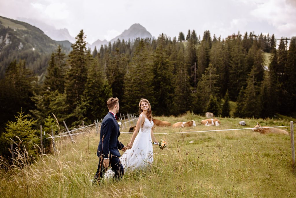 Braut und Bräutigam streifen Hand in Hand durch eine Wiese in den Garmischer Alpen vor dem Kreuzjochhaus